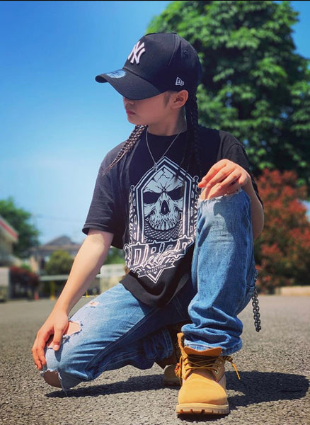 Person wearing a black cap, graphic t-shirt, and ripped jeans outdoors on a sunny day.